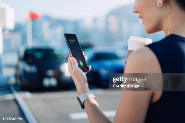 over the shoulder view of young asian businesswoman having coffee to go, using ai assistant on smartphone while walking to her car in carpark in downtown district in the city. business on the go and technology concept - speech recognition stock pictures, royalty-free photos & images