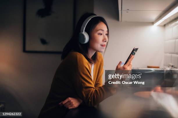 young woman with bluetooth headphones listening to music on smartphone - listening stockfoto's en -beelden