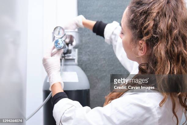 young female scientist opening a gas cylinder with pressure gauge in a specialized laboratory. laboratory research concept. - hydrogen stockfoto's en -beelden