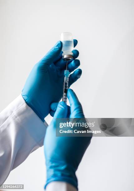 hands in gloves drawing vaccine into syringe on white background. - blue glove stock pictures, royalty-free photos & images