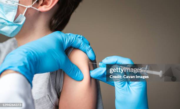 child wearing mask getting vaccinated by doctor holding a needle. - mmr bildbanksfoton och bilder