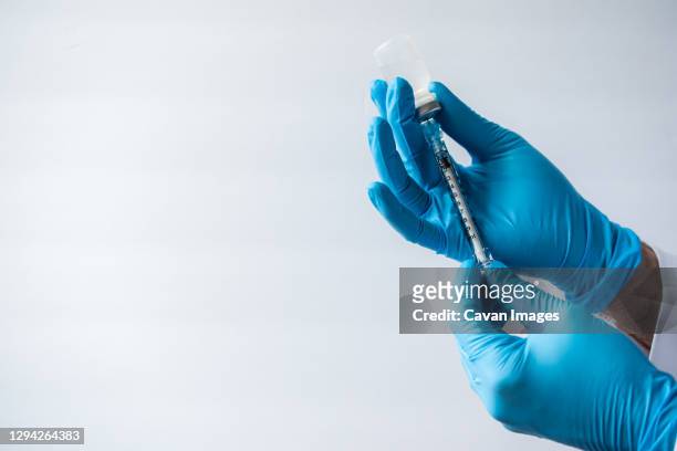 hands in gloves drawing vaccine into syringe on white background. - covid 19 vaccine stock pictures, royalty-free photos & images