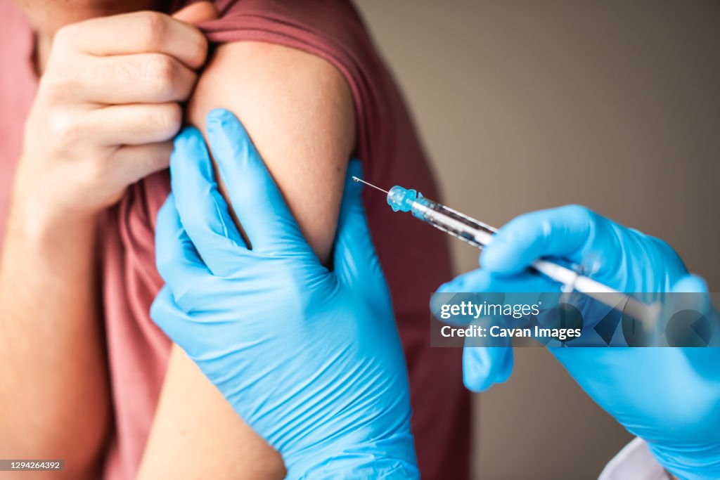 Close up of arm of boy getting vaccinated by doctor holding a needle.