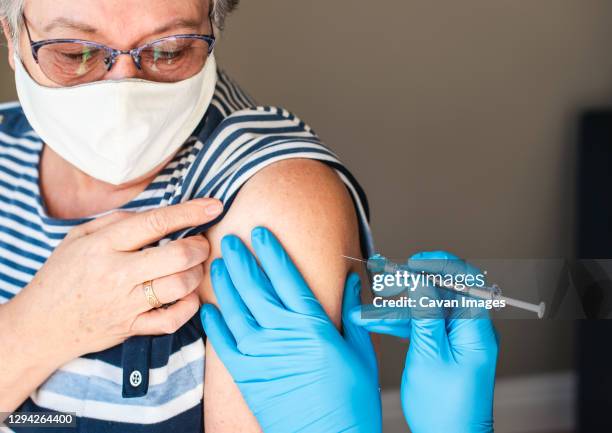 close up of older woman getting injected with a vaccine in upper arm. - gordelroos stockfoto's en -beelden