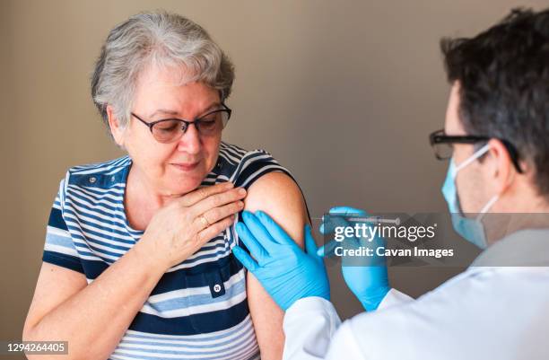 older woman getting injected with a vaccine by doctor in upper arm. - bältros bildbanksfoton och bilder