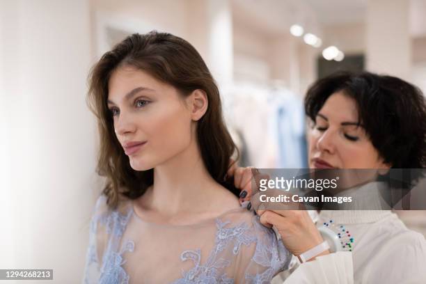 charming woman trying on tailor made dress with female assistant - clothes customization stockfoto's en -beelden