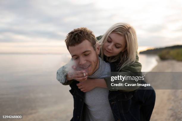 loving millennial couple smoking joint strolling on cold seashore - smoking weed stock-fotos und bilder