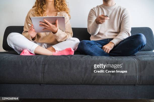 crop couple resting on sofa using tablet and tv remote - television show stock-fotos und bilder