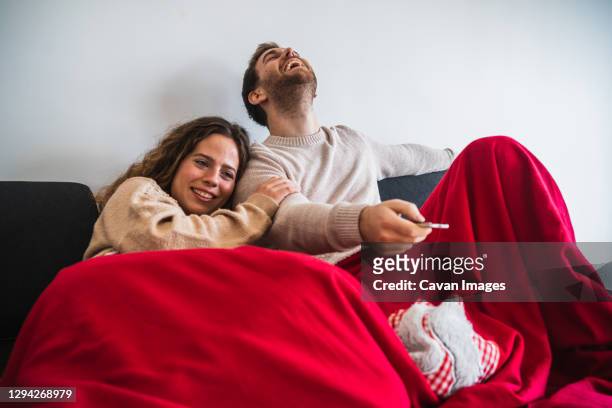 cheerful man and woman watching tv covered with blanket - television show foto e immagini stock