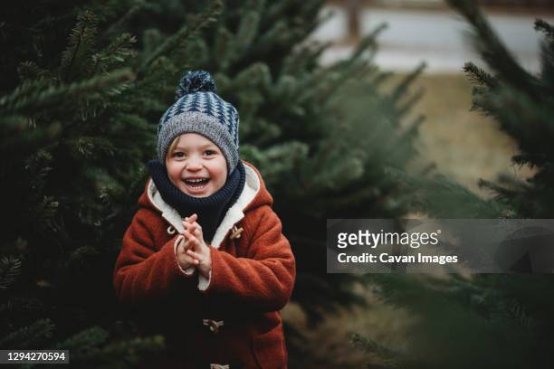 child smiling at tree farm picking one for christmas wearing wool - christmas hat stockfoto's en -beelden