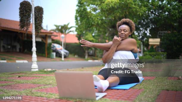 femme aîné observant la classe d’exercice dans l’ordinateur portatif à la maison avant ou arrière - fitness or vitality or sport and women photos et images de collection