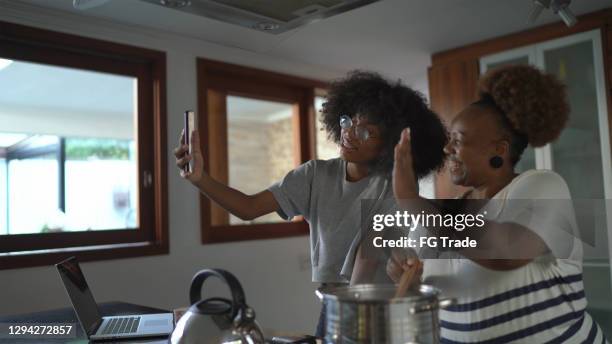 mother and daughter cooking and doing video chat on smartphone together at home - virtual lunch stock pictures, royalty-free photos & images