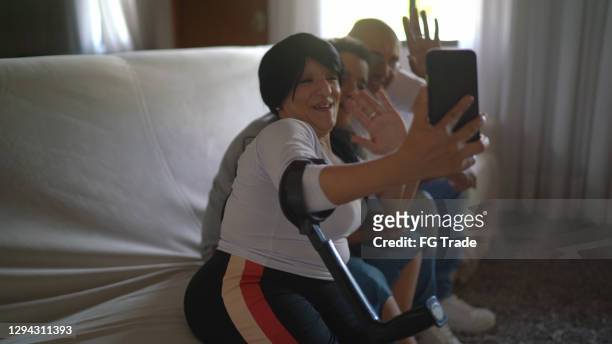 familia en el sofá haciendo una videollamada en el teléfono inteligente en casa - incluyendo una madre enana - plano fijo fotografías e imágenes de stock