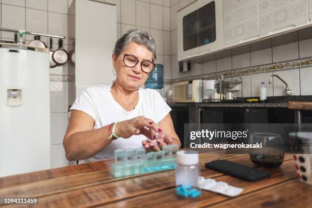 senior woman putting medications in a daily pill organizer - pill organizer stock pictures, royalty-free photos & images