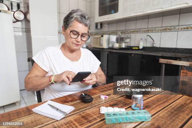 femme aîné enregistrant son niveau de sucre dans le sang avec un smartphone - blood sugar test photos et images de collection