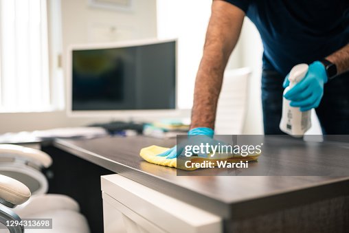 Hombre desinfectando un escritorio de oficina Hombre desinfectando un escritorio de oficina