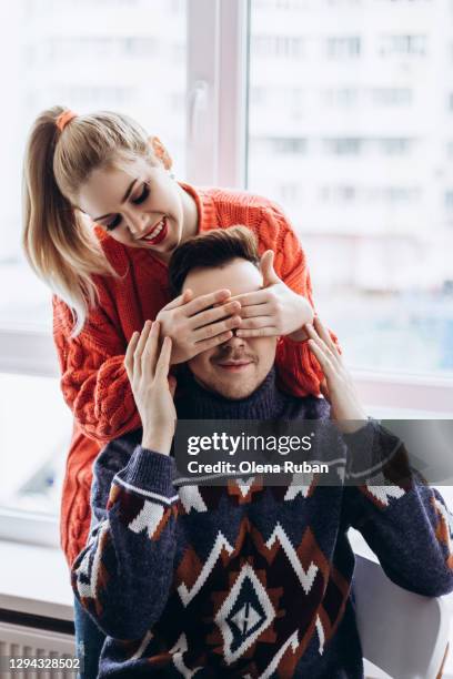 young woman in a sweater closes the eyes of a man - woman smiling eyes closed stock pictures, royalty-free photos & images