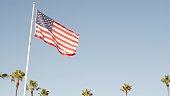Palms and american flag, Los Angeles, California USA. Summertime aesthetic of Santa Monica and Venice Beach. Star-Spangled Banner, Stars and Stripes. Atmosphere of patriotism in Hollywood. Old Glory