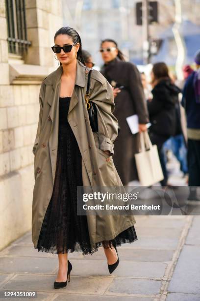 Fiona Zanetti wears sunglasses, Dior earrings, a light khaki trench coat, a black glossy patent-leather Dior bag, a black mesh tulle dress with a...