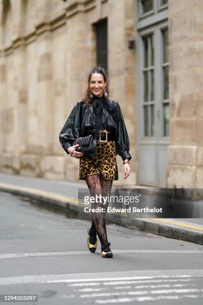 Alba Garavito Torre wears long golden shiny earrings, a black leather gathered oversized shirt / jacket with puff sleeves from Munthe, a black mesh...