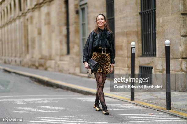 Alba Garavito Torre wears long golden shiny earrings, a black leather gathered oversized shirt / jacket with puff sleeves from Munthe, a black mesh...