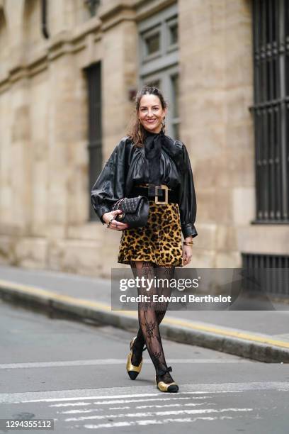 Alba Garavito Torre wears long golden shiny earrings, a black leather gathered oversized shirt / jacket with puff sleeves from Munthe, a black mesh...