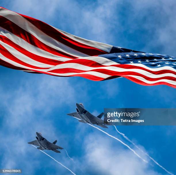 american-flag-blowing-in-wind-and-lockheed-martin-f-22-raptors-flying-against-sky.jpg
