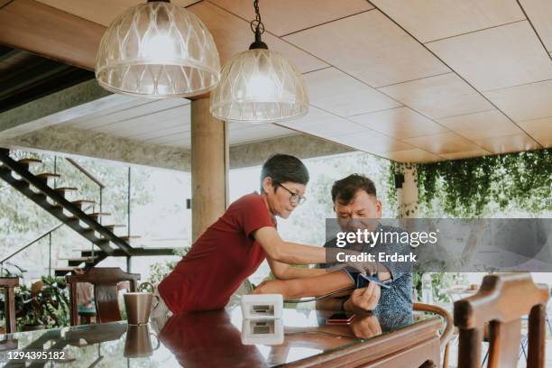 elderly couple are checking and talking with blood pressure at home- stock photo - asian wife stock pictures, royalty-free photos & images