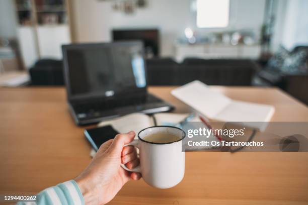 personal perspective of hand holding a cup of coffee in front of a table with planning items - hand resting on wood stock-fotos und bilder