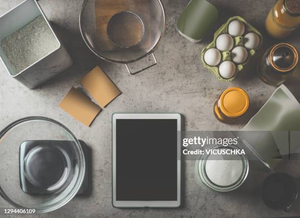 modern tablet pc on kitchen table with various bake ingredients: flour, eggs, sugar and packaging products and glasses. - bakery display stock-fotos und bilder