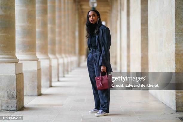 Emilie Joseph wears long bejeweled earrings from Isabel Marant, a black turtleneck pullover from Uniqlo, a dark navy blue striped oversized blazer...