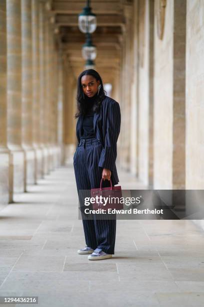 Emilie Joseph wears long bejeweled earrings from Isabel Marant, a black turtleneck pullover from Uniqlo, a dark navy blue striped oversized blazer...