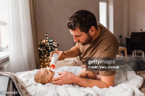 family, parenthood and people concept - father feeding little daughter with baby formula from bottle at home - eltern baby stockfoto's en -beelden