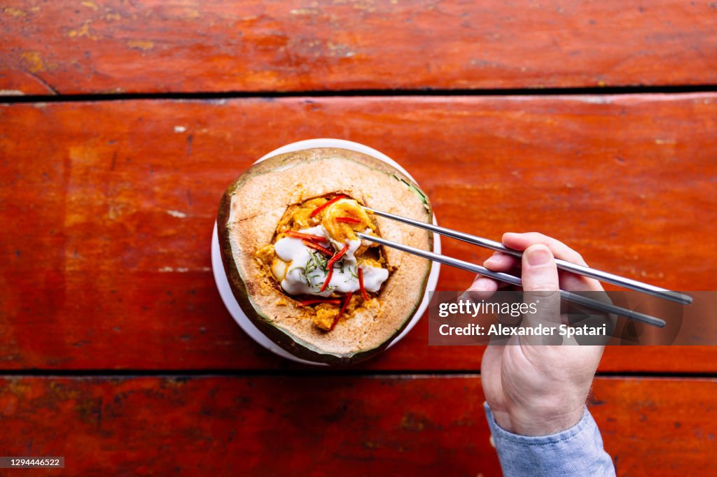 Man eating shrimps curry from green coconut bowl, personal perspective view