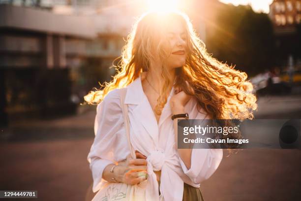 portrait of happy successful woman with tousled hair in city at sunset - curly blonde hair stock pictures, royalty-free photos & images