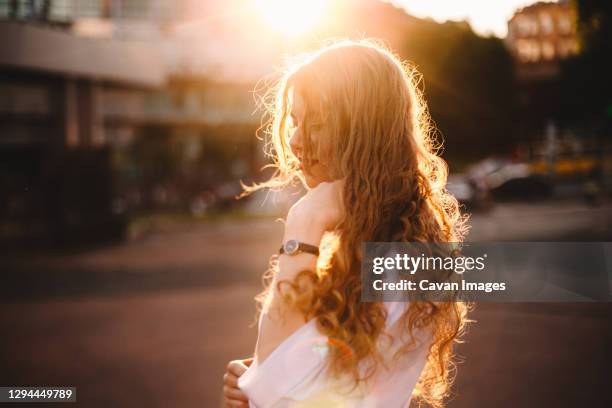 portrait of happy young woman standing in city at sunset - curly blonde hair stock pictures, royalty-free photos & images