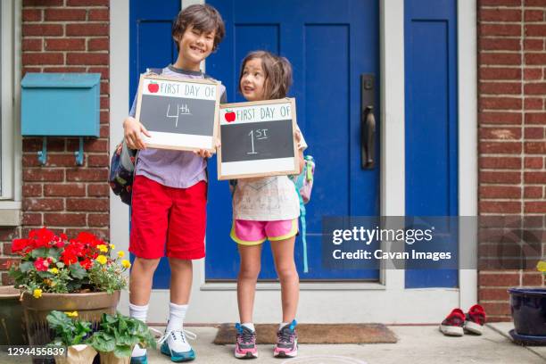 two siblings stand together on stoop holding first day of school signs - first day of school stock-fotos und bilder