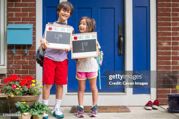 two siblings stand together on stoop holding first day of school signs - eerste-schooldag stockfoto's en -beelden