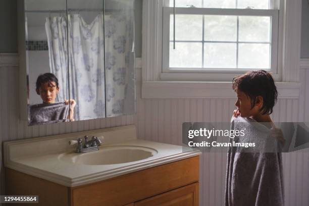 a boy stands in front of shower wrapped in a towel looking in a mirror - boys taking a shower stock pictures, royalty-free photos & images