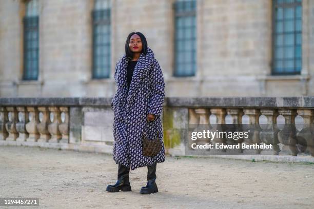 Carrole Sagba wears a long winter puffer coat with printed monograms from Saks Potts, a black pullover from Acne Studios, a brown monogram print...