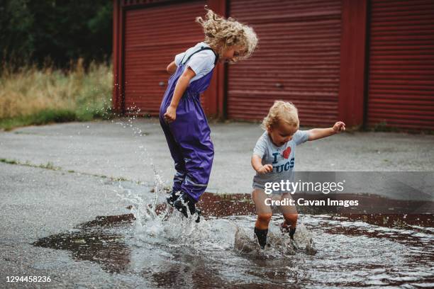 brother and sister jumping in a big puddle having fun and laughing - brother sister shower stock-fotos und bilder