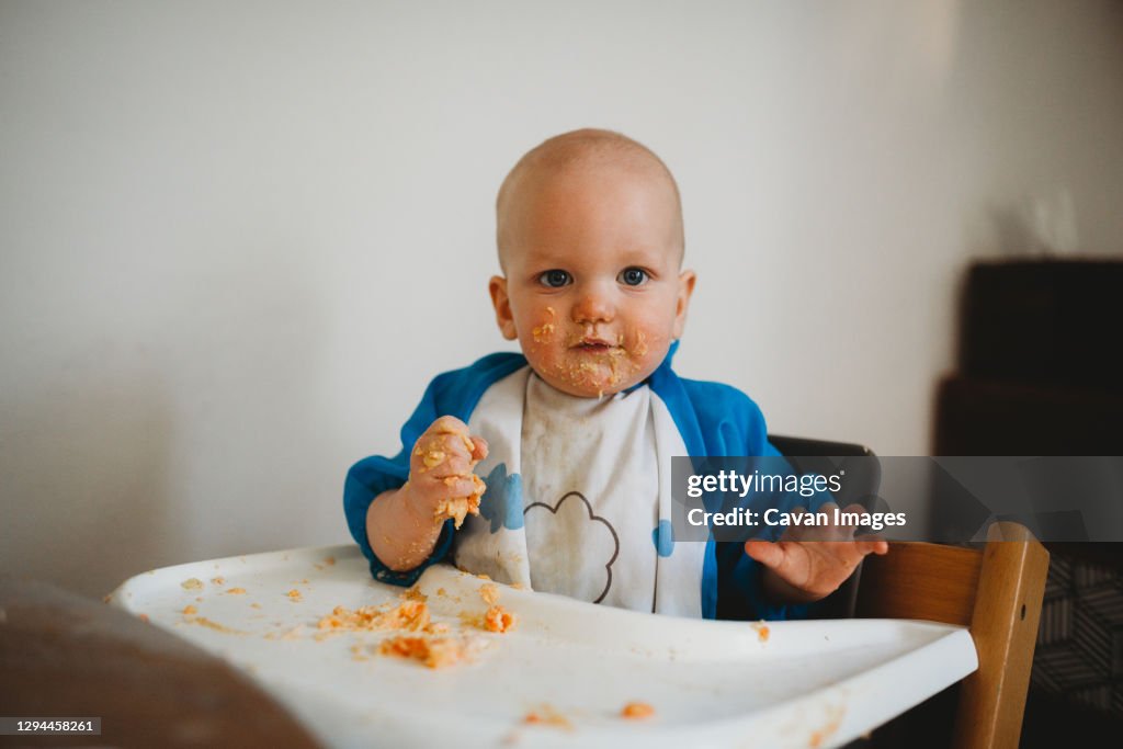 Baby boy eating with his hands making a mess with food all over face