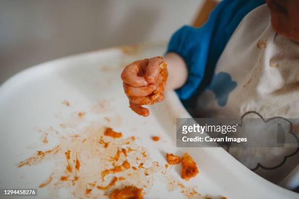 close up of a baby's hands while eating and making a mess - high chair stock pictures, royalty-free photos & images