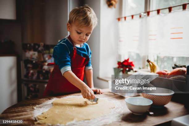 young child making christmas cookies in the kitchen at home with apron - flour christmas photos et images de collection