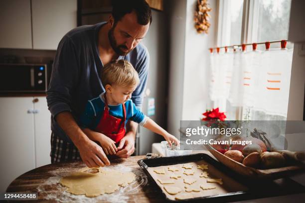 father and son in kitchen at home baking christmas cookies in pajamas - faire cuire au four photos et images de collection
