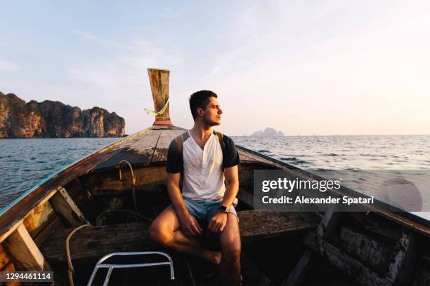 young man traveling on a long-tail boat in thailand - longtail boat stock pictures, royalty-free photos & images