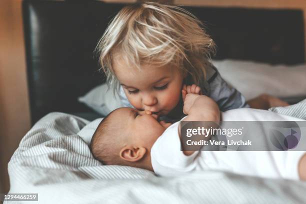 little brother hugging his newborn sister. toddler kid meeting new sibling. cute boy and new born baby girl relax in a white bedroom. family with children at home. love, trust and tenderness - kiss sisters foto e immagini stock
