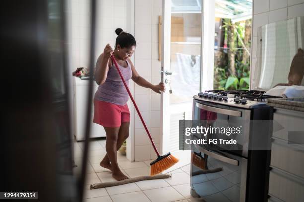 rijpe vrouw die keukenvloer veegt - huishoudelijke dienstverlening stockfoto's en -beelden