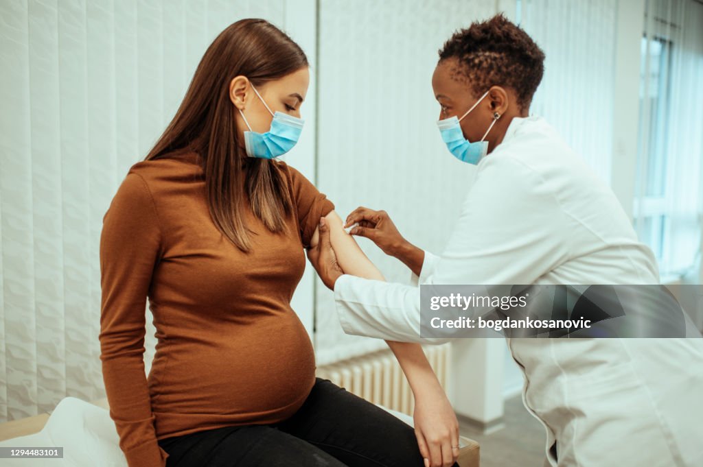 African American female doctor preparing a pregnant woman for vaccination