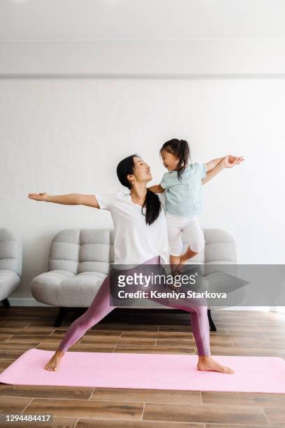 young asian mom and her daughter doing yoga in the living room - child mental health wellness stock-fotos und bilder